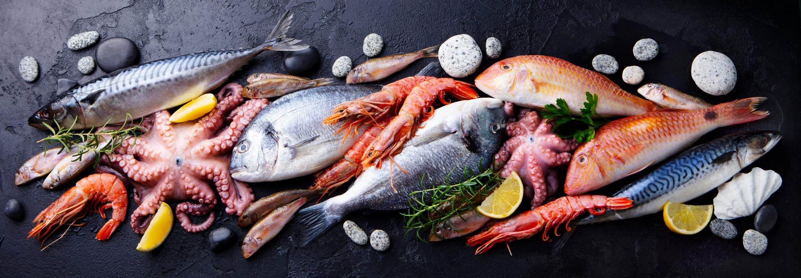 Fresh fish and seafood assortment on black slate background